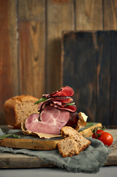 A piece of delectable ham paired with basil leaves, ripe tomatoes, and fresh bread elegantly arranged on a rustic wooden platter. Image for the food selling company. Serving dishes. Food Inspiration.