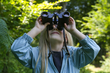 Cute little girl exploring nature looking through binoculars. Child playing outdoors. Kids travel, adventure and bird watching concept.