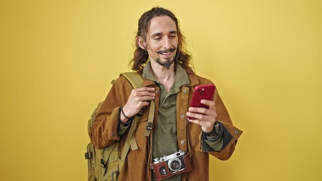 Young hispanic man tourist using smartphone over isolated yellow background