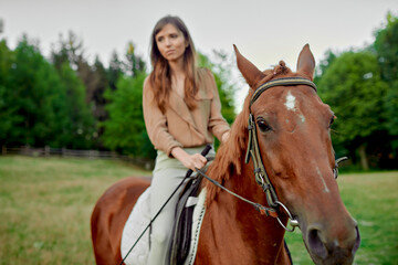 Obraz premium Equine expedition. A charming female rider in beige blouse on her brown horse. Bond with animals, de-stress, and explore nature for emotional well-being. Emotion-filled horse riding lesson gift