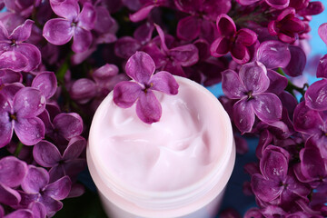 Jar of cream and lilac beautiful flowers as background, closeup