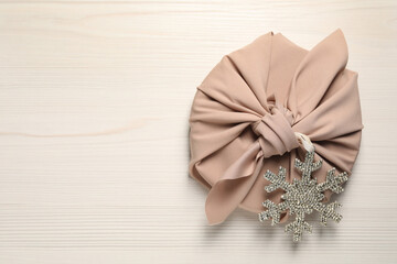 Furoshiki technique. Gift packed in pink fabric and decorative snowflake on white wooden table, top view. Space for text