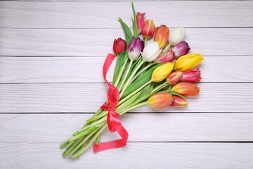 Bouquet of beautiful colorful tulip flowers tied with red ribbon on white wooden table, top view