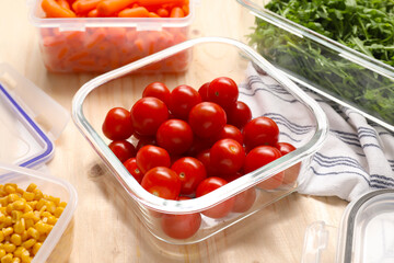 Containers with tomatoes and fresh products on wooden table, closeup. Food storage