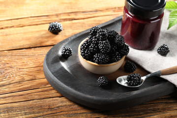 Fototapeta na wymiar Fresh ripe blackberries and tasty jam on wooden table. Space for text