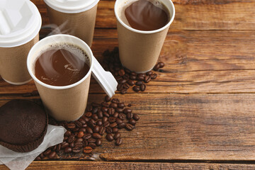 Coffee to go. Paper cups with hot drink, tasty chocolate muffin and beans on wooden table. Space...