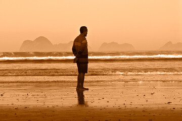 Fototapeta premium The man standing on the beach at sunset