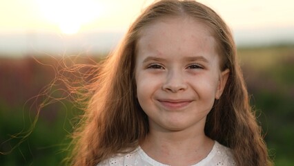 Adorable little girl looks in camera playing in country field against gentle sunset
