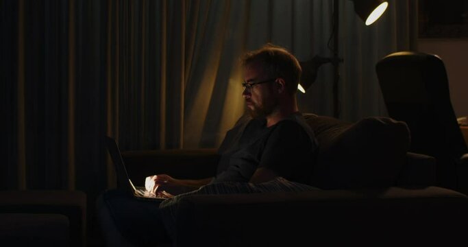 A workaholic man works on his laptop late at night and slowly looks up