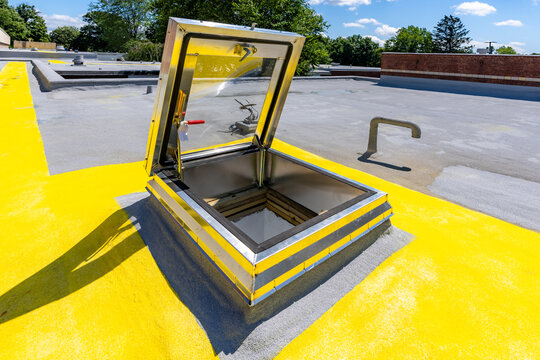 Roof hatch for access to roof with a built in skylight on a spray foam roof with painted yellow walking path

