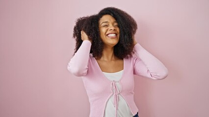 African american woman smiling confident combing hair with hands over isolated pink background