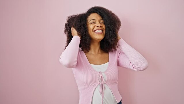 African american woman smiling confident combing hair with hands over isolated pink background