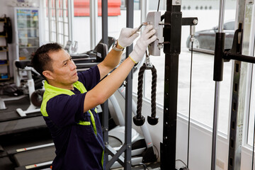 Professional Asian male service worker or fitter checks equipment, maintains and secures fitness...