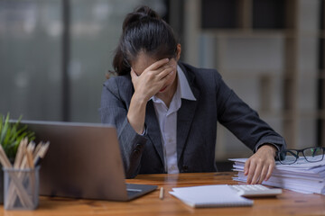 Portrait of tired young business Asian woman work with documents tax laptop computer in office. Sad, unhappy, Worried, Depression, or employee life stress concept	