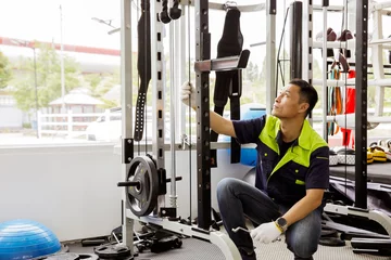Foto op Plexiglas Fitness Professional Asian male service worker or fitter checks equipment, maintains and secures fitness equipment in indoor gym, provides safety for users : Skilled technicians repair exercise machines.