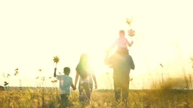 happy family mother father son daughter walking park sunset. silhouette large family children. hold hand. teamwork. group people sunset field. family travel children glare sunlight. pinwheel hand toy.