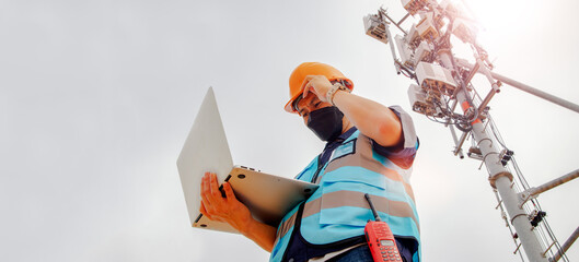 Helmeted asian male engineer works field with telecommunication tower that controls mobile...