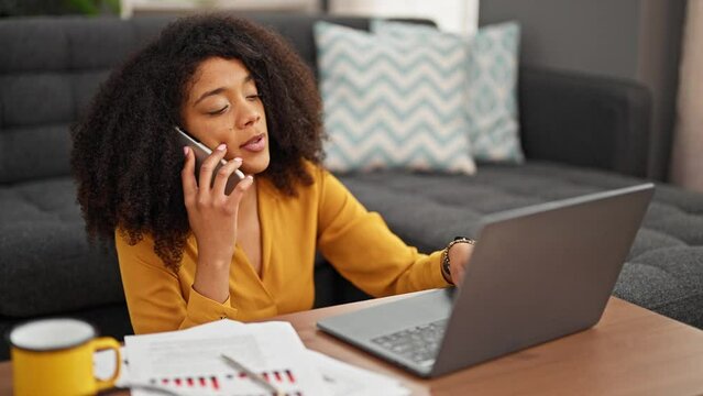 African american woman talking on smartphone taking notes working at home