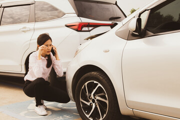 Asian woman sits stressed and worried as her reckless driver hits the back of her car and damages...