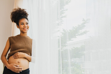 Pregnant new mom Thai-African descent stands near window at home first pregnant mom happy and in a...