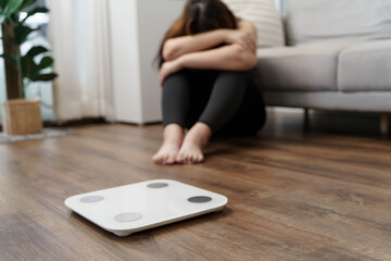 Fototapeta premium Sad woman with fat upset bored of dieting Weight loss fail&nbsp; Fat diet and scale sad asian woman on weight scale at home weight control