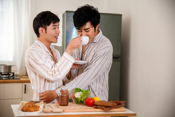 Happy gay couple enjoy breakfast in kitchen drinking coffee. Two best friends LGBTQ relation partner home cooking. Happiness romance homosexual marriage lifestyle. Two men together love friendship.