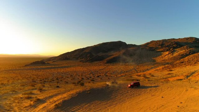 Aerial Descending Forward Towards Car And Dune Buggy By Smoke In Desert At Sunset - Mohave Desert, California
