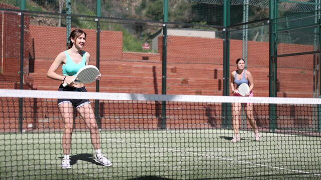 Two young sporty girls playing padel game in court on sunny day 