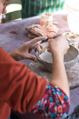 detail of the hands of a caucasian woman shaping a clay bowl with a tool