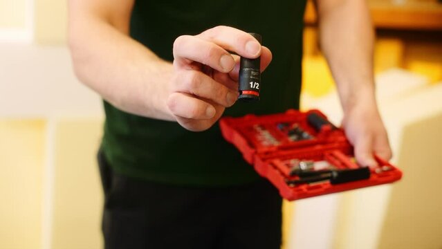 A Young man carpenter inside his workshop shows the different drill bits that come in a professional set of tools.