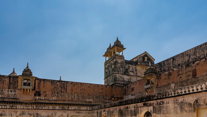 Weathered sandstone wall of the ancient Amber Fort. Watchtowers with domes and columns against a...