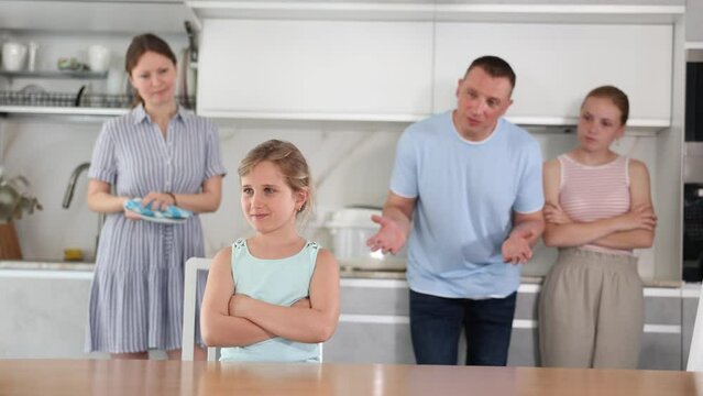 At kitchen parents scold standing daughter for bad behavior, mother clean dish in background. High quality 4k footage