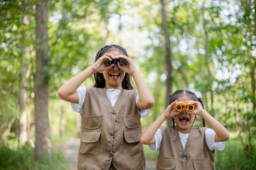 Happy Little Asian girls looking ahead and smiling child with the binoculars in the park. Travel...