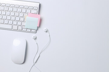 White bright composition on modern office desk with keyboard, wireless mouse, earphones and blank sticky notes. 