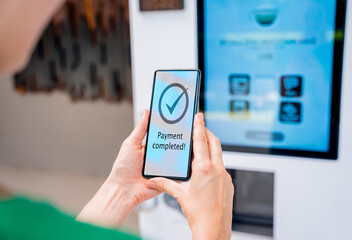 Young woman paying for coffee at vending machine using contactless method of payment 