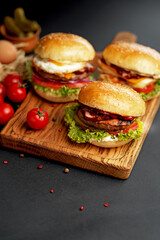 Close-up of a delicious fresh homemade burger with lettuce, cheese, onion and tomato on a rustic wooden board on a dark background