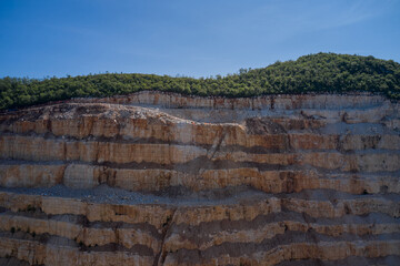 Steps of a marble quarry in the background green forest blue sky. Panorama Large marble quarry against the blue sky. Open pit marble extraction.