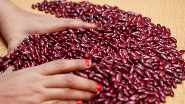 A hand picks up red beans from a wooden table
