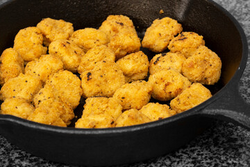 Spicy coated southern fried chicken bites in a cast iron frying pan. On a black granite background