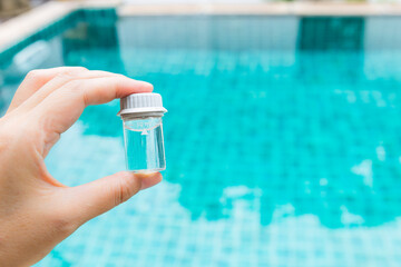 Water sample tube in girl hand with space on blurred swimming pool background, water test and...