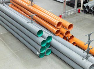 PVC plastic pipes and tubes stacked in warehouse. Choosing a sewage pipe from pipes store and...