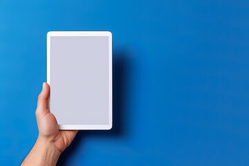 Hand holding tablet with mockup blank screen isolated on blue background with copy space