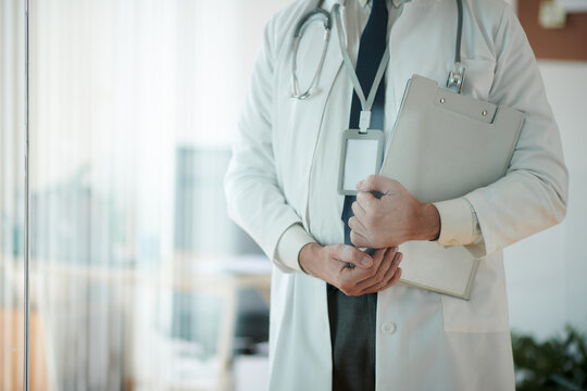 Cropped image of doctor in labcoat standing in medical office and holding clipboard