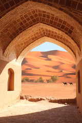 Ancient arch at the entrance to desert. View of sand dunes through stone arch. Travel, resort, vacation and holiday concept. Beautiful desert landscape with sand dunes and camel - obrazy, fototapety, plakaty