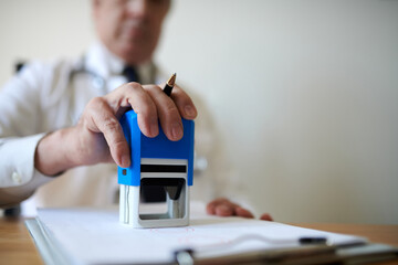 Closeup image of head of clinic putting stamps on documents and contracts
