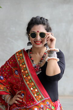 Indian woman in a stylish traditional look for Navratri for playing Garba and dandiya wirh sun glasses and fabric and oxidized jewelry. red and black outfit with traitional bangles earings, bindi.