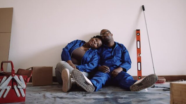 Black Couple in Blue Overalls Sitting on the Floor Head on Shoulder