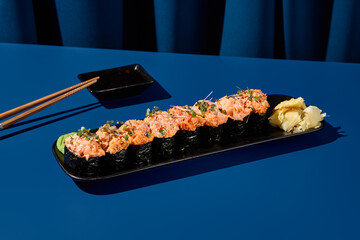 Exquisite gunkan sushi set featuring crab, shrimp, salmon, tuna, and eel, elegantly displayed on a black plate against a vivid blue curtain backdrop