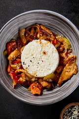 A top view of a grey bowl filled with Chinese-style seafood rice, presented on a black background with chopsticks and sesame seeds scattered around the table
