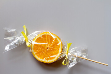 Orange slice on stick wrapped in foil, fruit lollipop, healthy substitute for sweets, creative concept